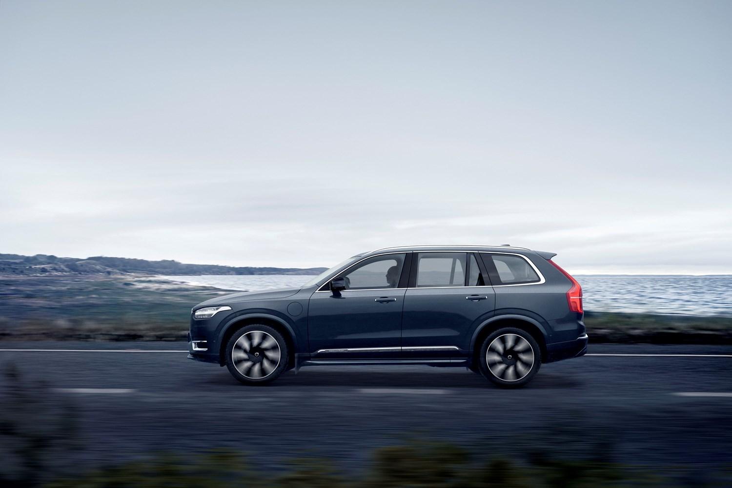 Side view of the new Volvo XC90 Recharge in black, driving on road with countryside and sea behind