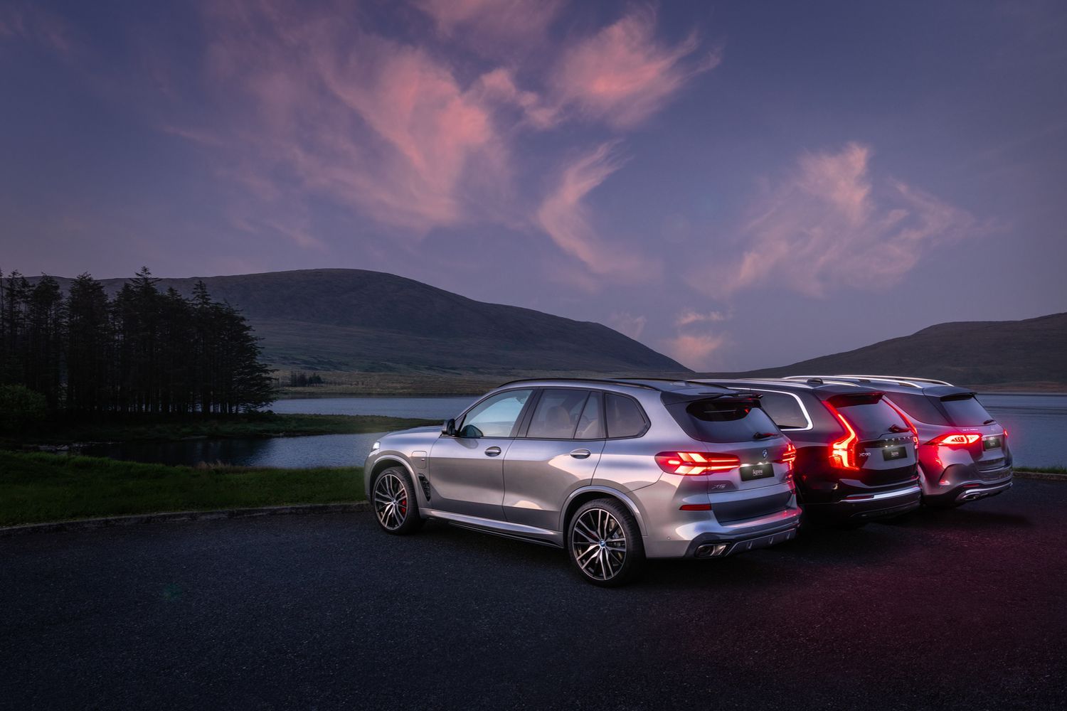 Rear and side view of three latest SUV models available at Agnew (Mercedes-Benz GLC, Q4 e-tron and a BMW X4), parked at scenic car park next to lake during sunrise.